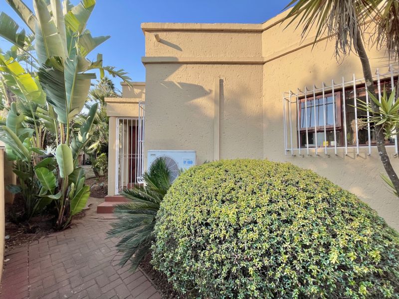 Rear exterior view of the property featuring a paved walkway, stucco wall finish, security bars on windows, and an external air conditioning unit.