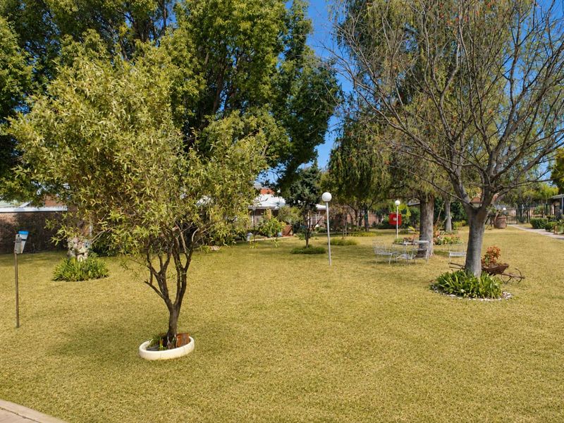 A spacious, well-maintained communal garden area featuring established trees, manicured lawn, and integrated garden lighting.