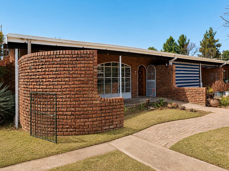 Front elevation of a townhouse featuring a distinctive curved brick wall, paved walkway, and a covered entrance area with security gate.