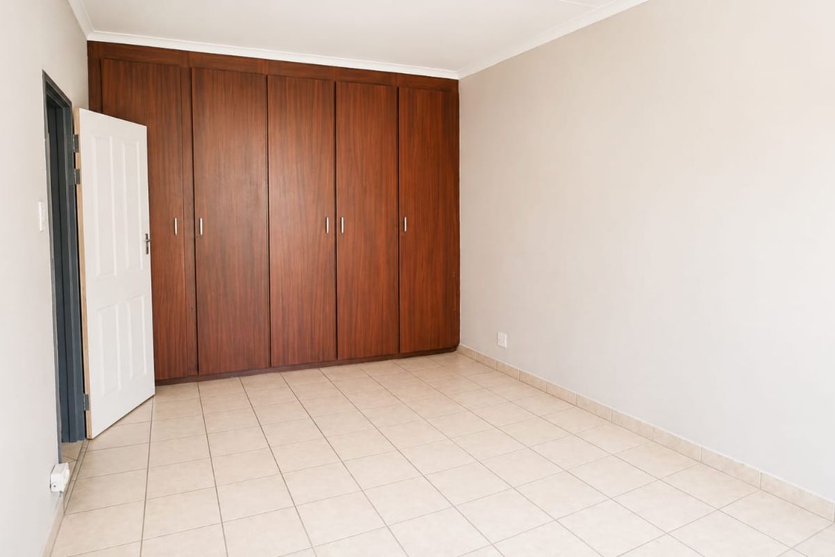 A clean, empty bedroom featuring neutral tiled flooring and extensive floor-to-ceiling built-in wooden cupboards.