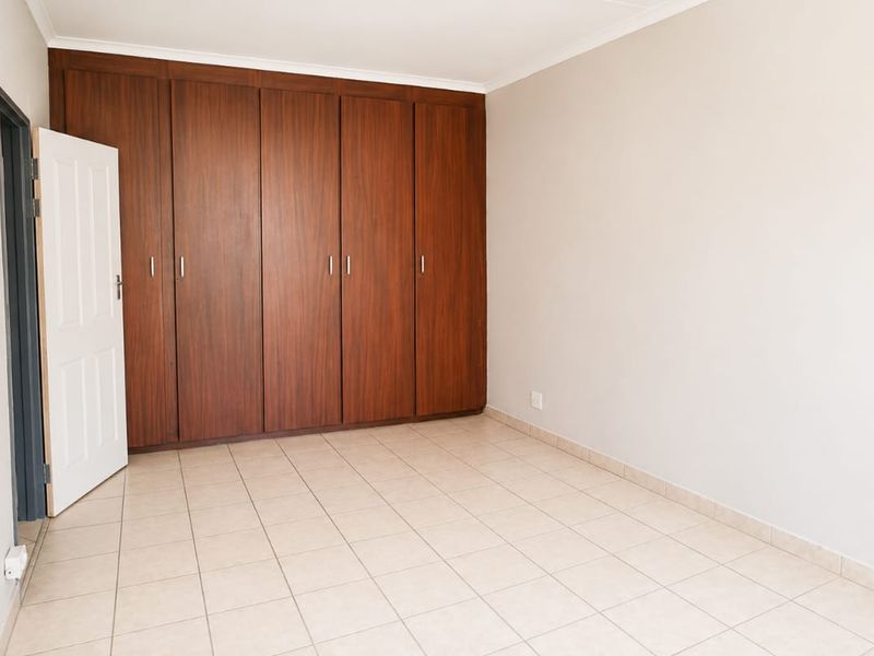 A clean, empty bedroom featuring neutral tiled flooring and extensive floor-to-ceiling built-in wooden cupboards.