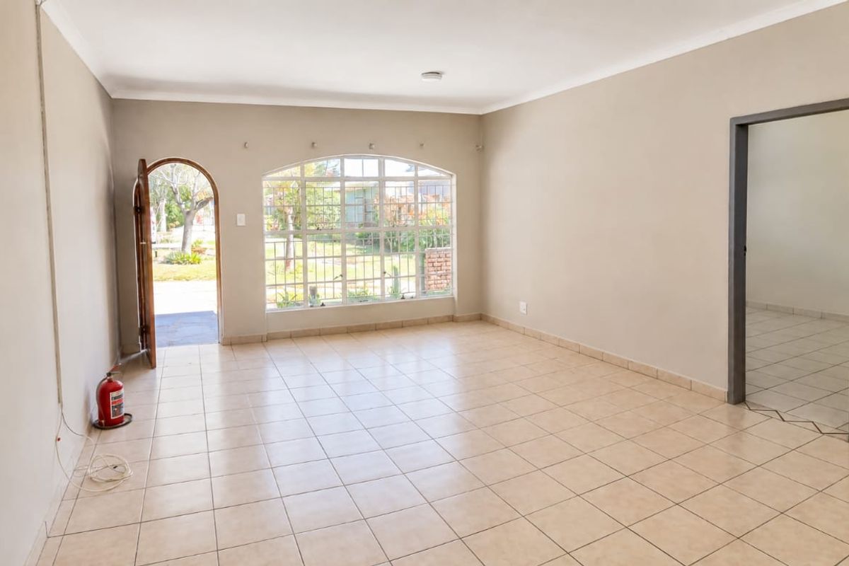 A spacious, empty living area featuring neutral tiled flooring, an arched entrance, and a large window with security bars, offering a bright and open layout.