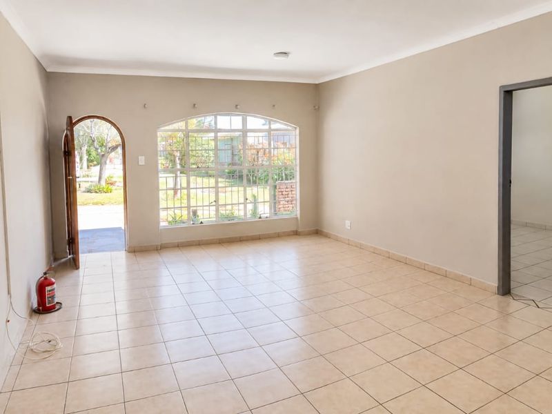 A spacious, empty living area featuring neutral tiled flooring, an arched entrance, and a large window with security bars, offering a bright and open layout.