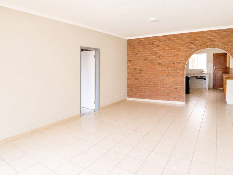 An open-plan living area featuring ceramic floor tiles, a prominent exposed brick feature wall with an arched opening, and neutral wall finishes.