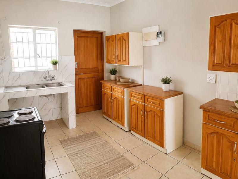 A functional kitchen featuring wooden cabinetry, tiled splashbacks, a double basin sink, and tiled flooring, offering a clean and practical workspace.