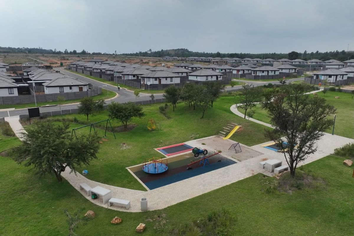 Aerial view of a residential estate featuring a communal park with playground equipment, paved walkways, and manicured green spaces.