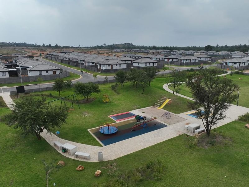 Aerial view of a residential estate featuring a communal park with playground equipment, paved walkways, and manicured green spaces.