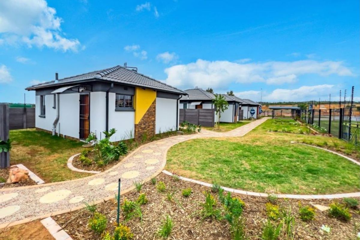A well-maintained residential exterior featuring a paved walkway, landscaped garden, and modern tiled roof homes with secure boundary walling.