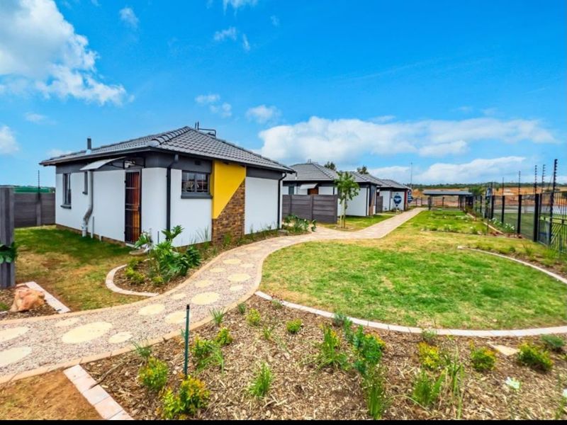 A well-maintained residential exterior featuring a paved walkway, landscaped garden, and modern tiled roof homes with secure boundary walling.