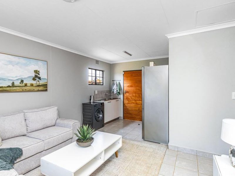 An open-plan living area featuring a compact kitchenette with a sink and tiled flooring, leading to an exterior timber door.
