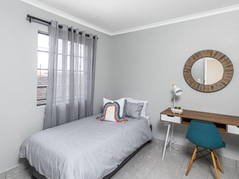 A well-maintained bedroom featuring neutral grey walls, tiled flooring, and a window with curtain fixtures.