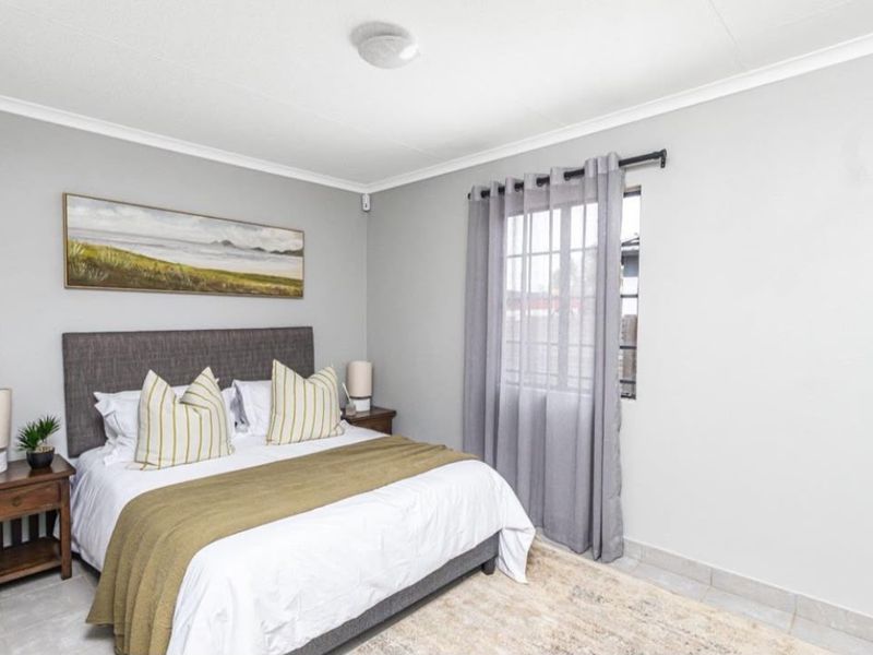 A well-maintained bedroom featuring neutral grey walls, tiled flooring, and a window with fitted curtain rod, providing a clean and comfortable living space.