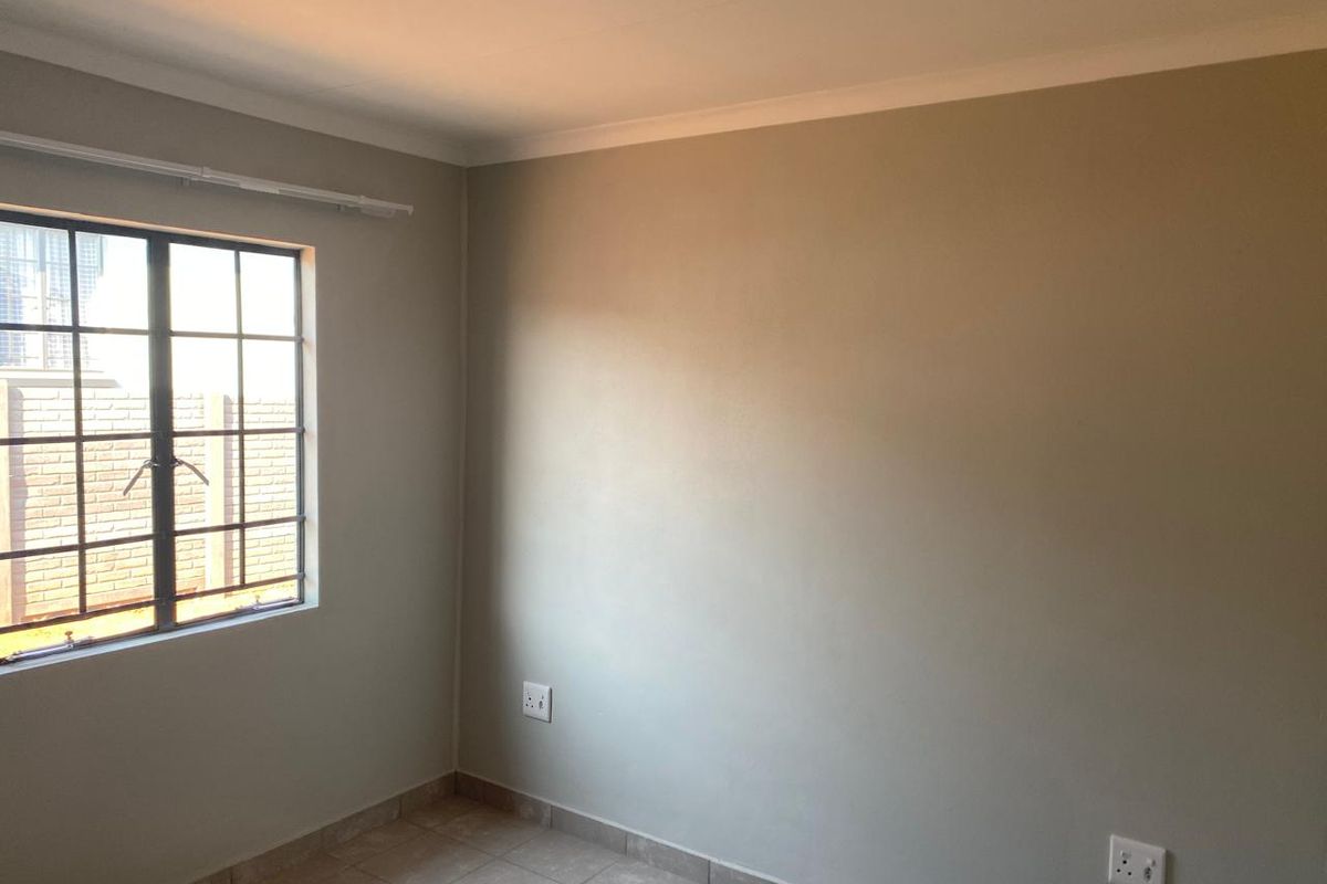 A clean, empty bedroom featuring neutral wall paint, tiled flooring, and a steel-framed window, providing a versatile space ready for personalization.