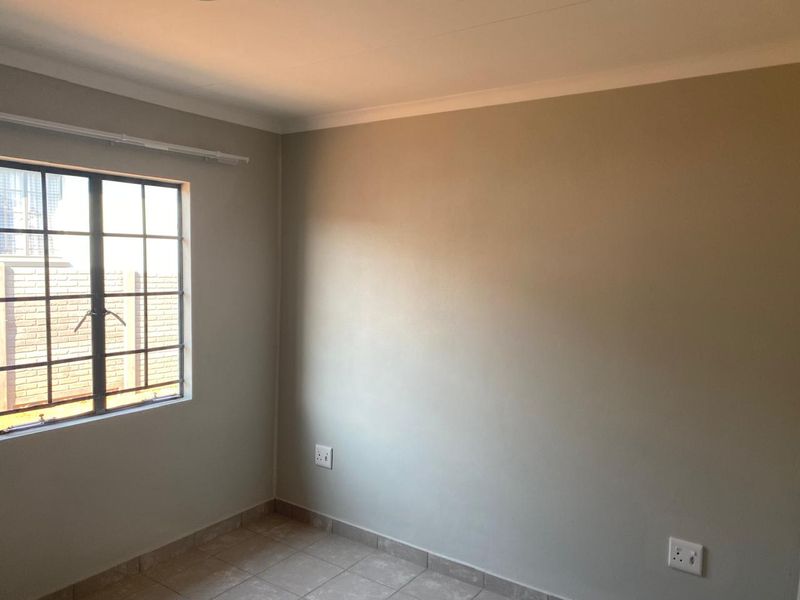 A clean, empty bedroom featuring neutral wall paint, tiled flooring, and a steel-framed window, providing a versatile space ready for personalization.
