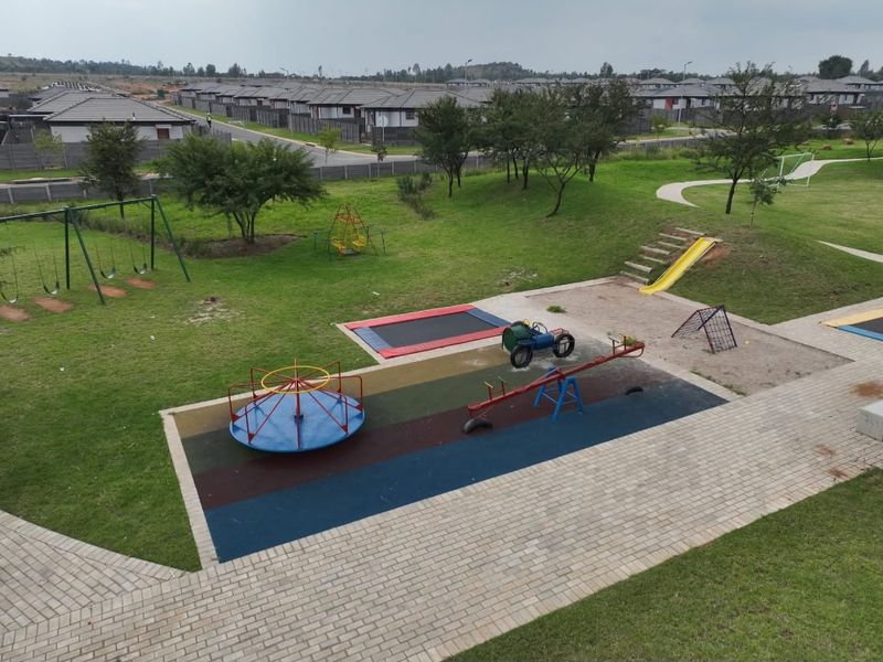 An elevated view of a well-maintained communal playground area featuring various play equipment, paved pathways, and landscaped green spaces within a residential estate.