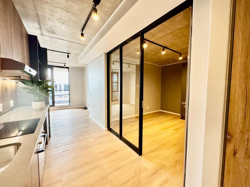 Modern open-plan apartment featuring an exposed concrete ceiling, sleek kitchen cabinetry, and a contemporary sliding glass partition separating the living and bedroom areas.