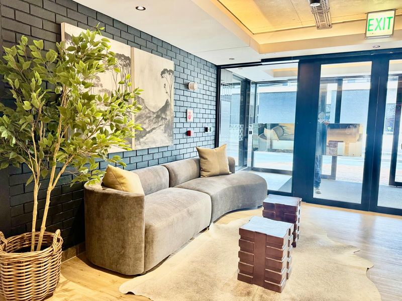 Modern apartment entrance lobby featuring a dark exposed brick feature wall, recessed lighting, and large glass doors providing natural light.