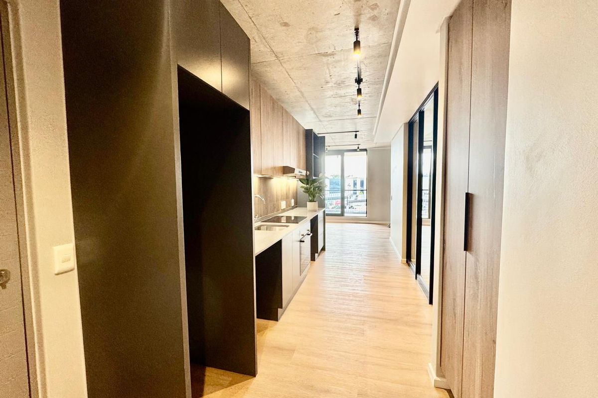 Modern galley-style kitchen featuring sleek built-in cabinetry, integrated appliances, exposed concrete ceilings, and high-quality laminate flooring in an open-plan layout.