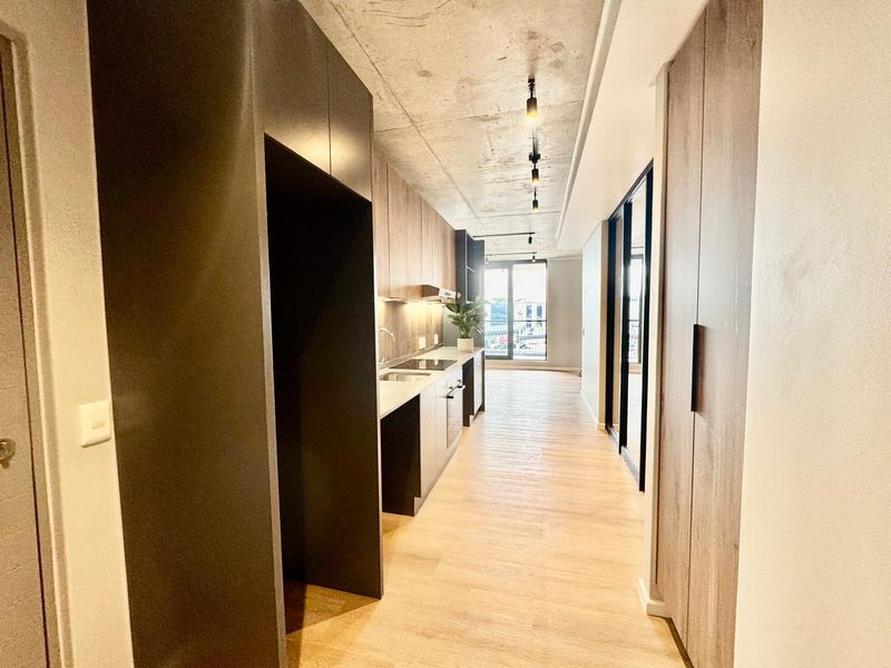 Modern galley-style kitchen featuring sleek built-in cabinetry, integrated appliances, exposed concrete ceilings, and high-quality laminate flooring in an open-plan layout.