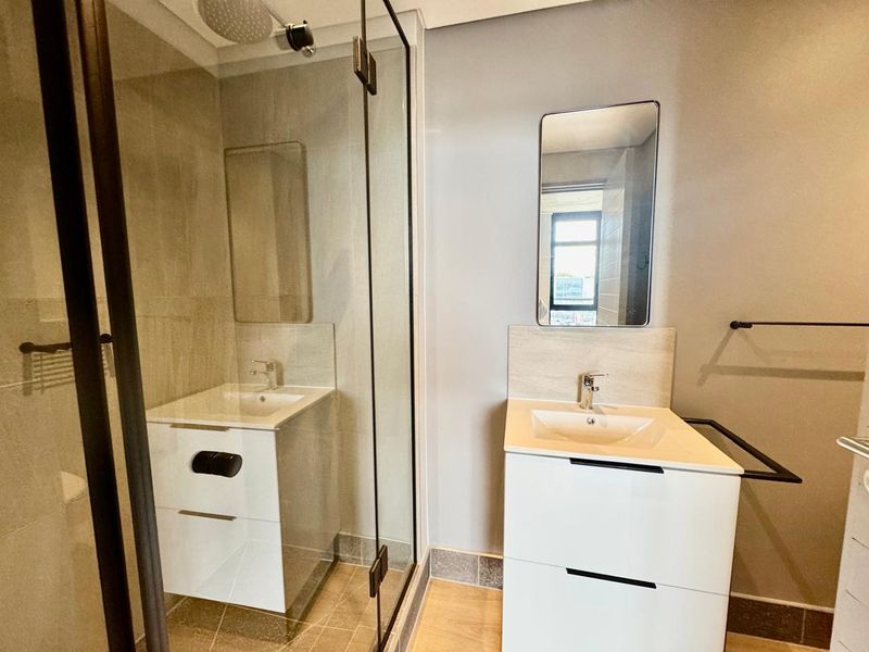 Modern bathroom featuring a glass-enclosed shower, contemporary vanity with basin, and wall-mounted mirror in a clean, neutral finish.