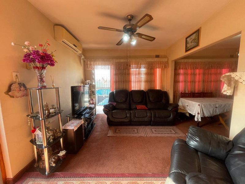 Open-plan living and dining area featuring carpeted flooring, a ceiling fan, and a wall-mounted split-system air conditioner with access to an outdoor balcony.