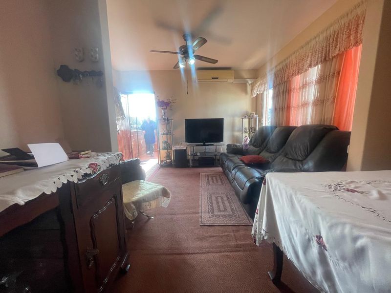 A living room featuring carpet flooring, a ceiling fan, and a wall-mounted split-system air conditioner, with direct access to an outdoor area.