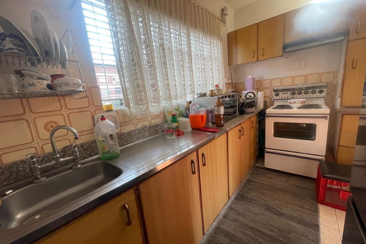 A functional galley-style kitchen featuring wood-look cabinetry, a stainless steel sink, and a freestanding electric stove with an integrated extractor fan.
