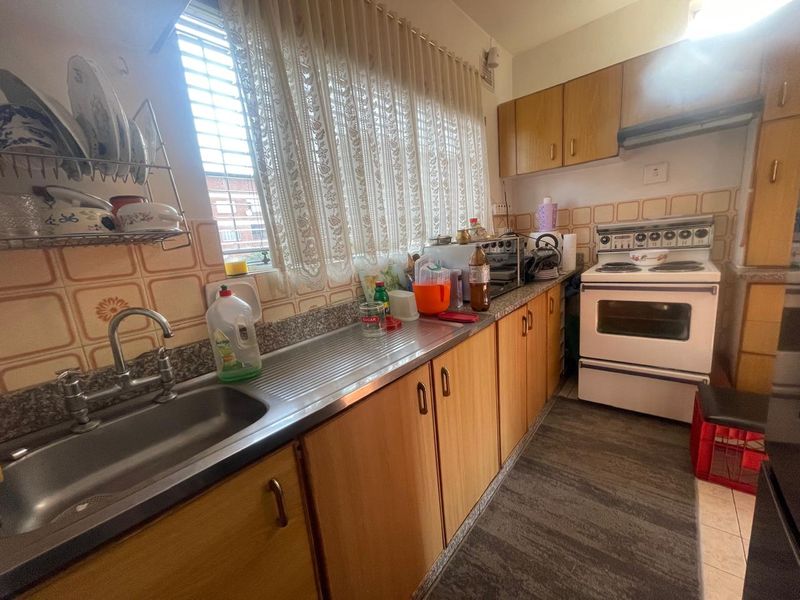 A functional galley-style kitchen featuring wood-look cabinetry, a stainless steel sink, and a freestanding electric stove with an integrated extractor fan.