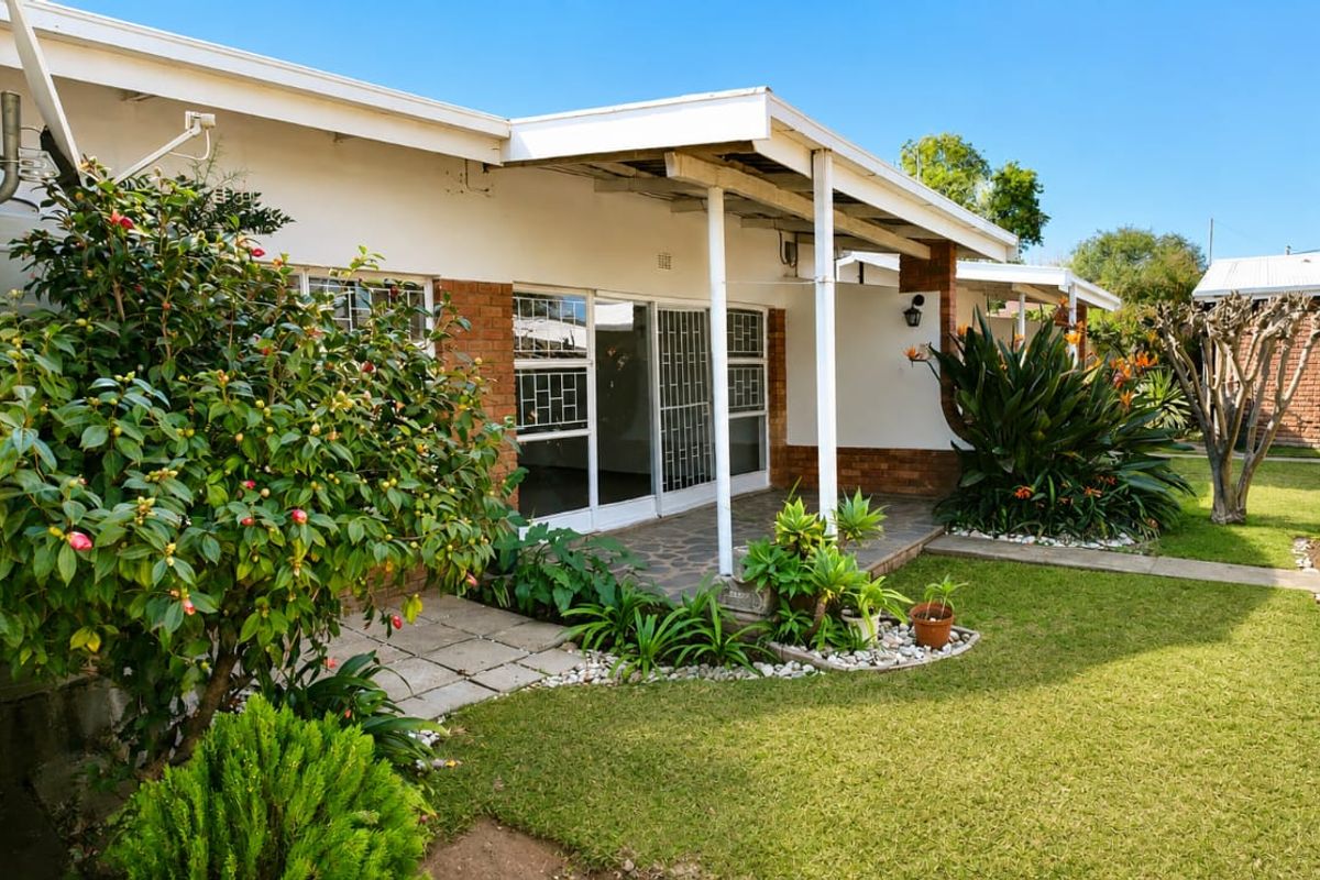 A rear view of the townhouse featuring a covered patio, sliding glass doors with security gates, and a well-maintained garden area.