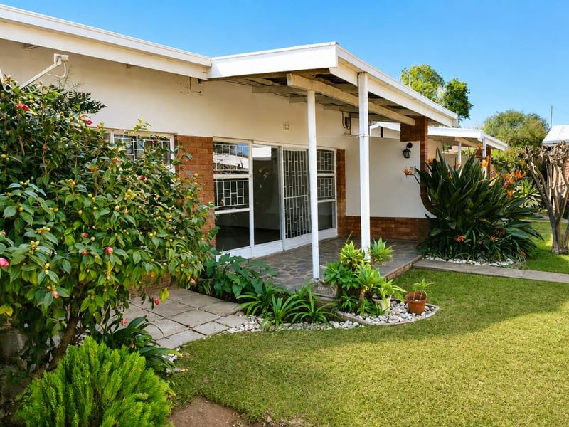 A rear view of the townhouse featuring a covered patio, sliding glass doors with security gates, and a well-maintained garden area.
