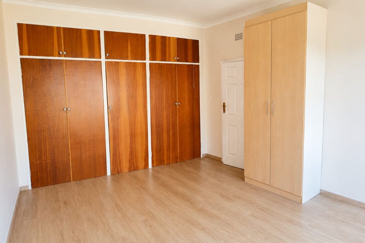 A bright, empty bedroom featuring wood-finish laminate flooring and extensive built-in cupboard storage.