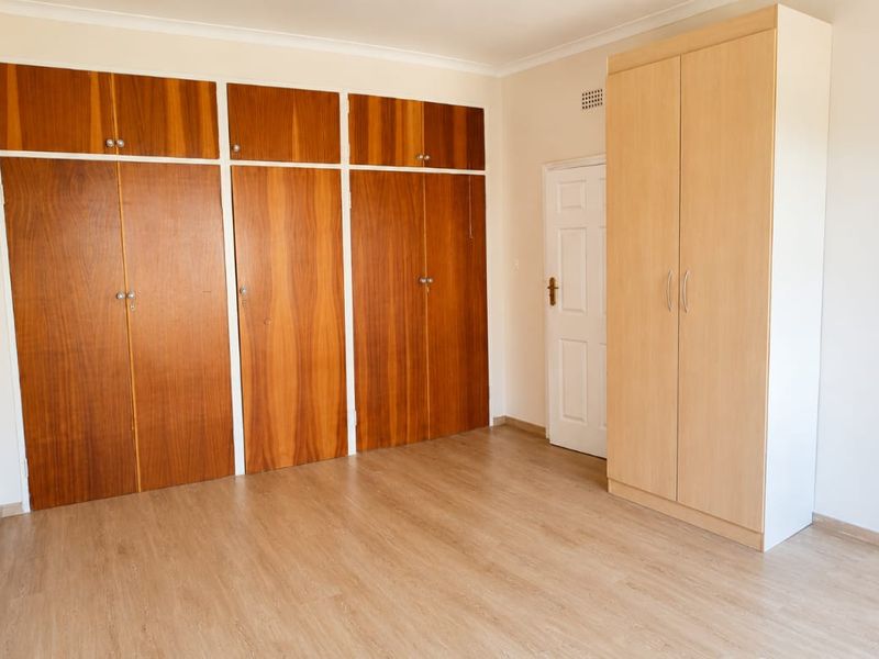 A bright, empty bedroom featuring wood-finish laminate flooring and extensive built-in cupboard storage.