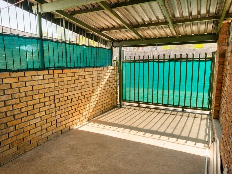 A covered outdoor patio area featuring brick walls, concrete flooring, and secure metal screening, providing a functional space for outdoor use.