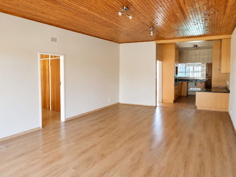 Spacious open-plan living area featuring timber ceiling and laminate flooring, flowing into a functional kitchen with built-in cabinetry and integrated oven.