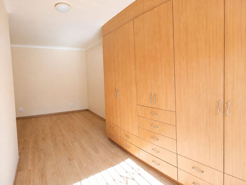 A bright, empty bedroom featuring extensive built-in wooden cupboards and light-toned laminate flooring, offering a clean and neutral space.