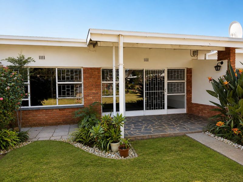 A well-maintained rear exterior view featuring a covered patio with stone paving, brick facade, and sliding glass doors leading into the home.