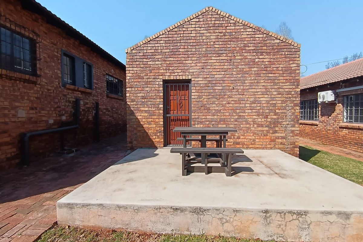 Rear exterior view featuring an exposed brick building facade, a concrete patio area, and a secure entrance gate.