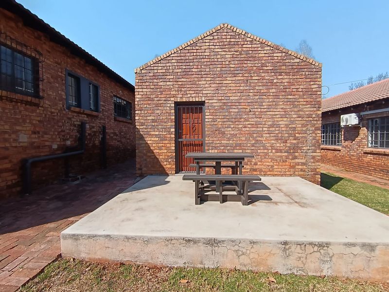 Rear exterior view featuring an exposed brick building facade, a concrete patio area, and a secure entrance gate.