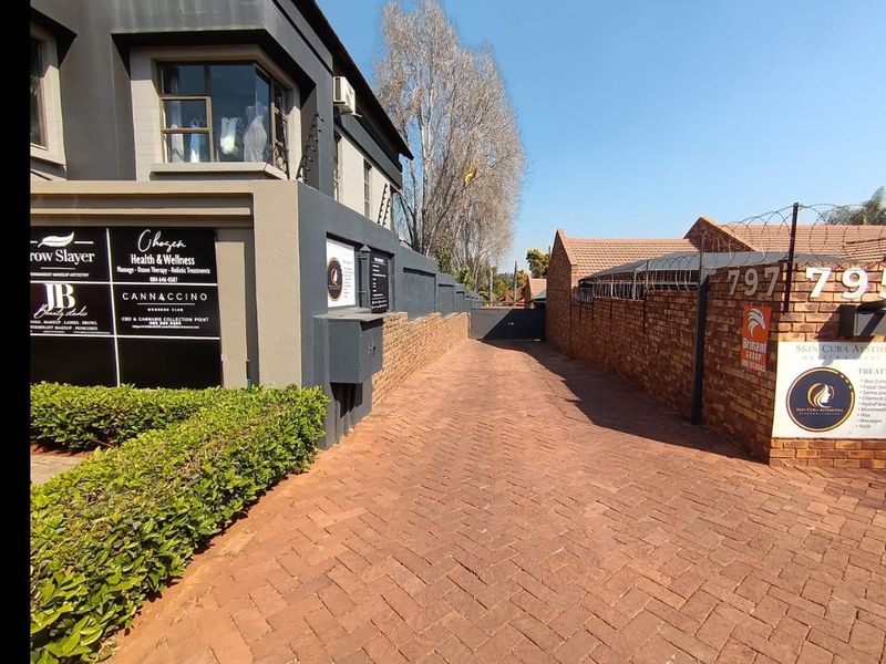 Commercial property entrance featuring a paved driveway, brick boundary walls with security fencing, and prominent business signage for multiple tenants.
