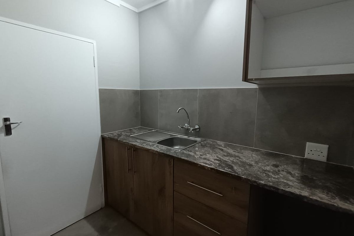 A functional kitchen area featuring built-in wooden cabinetry, a stainless steel sink, and a modern tiled backsplash.