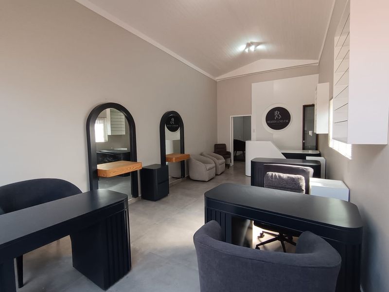 A well-maintained commercial salon space featuring arched wall mirrors, floating vanity shelves, a reception area, and neutral tiled flooring under a vaulted ceiling.