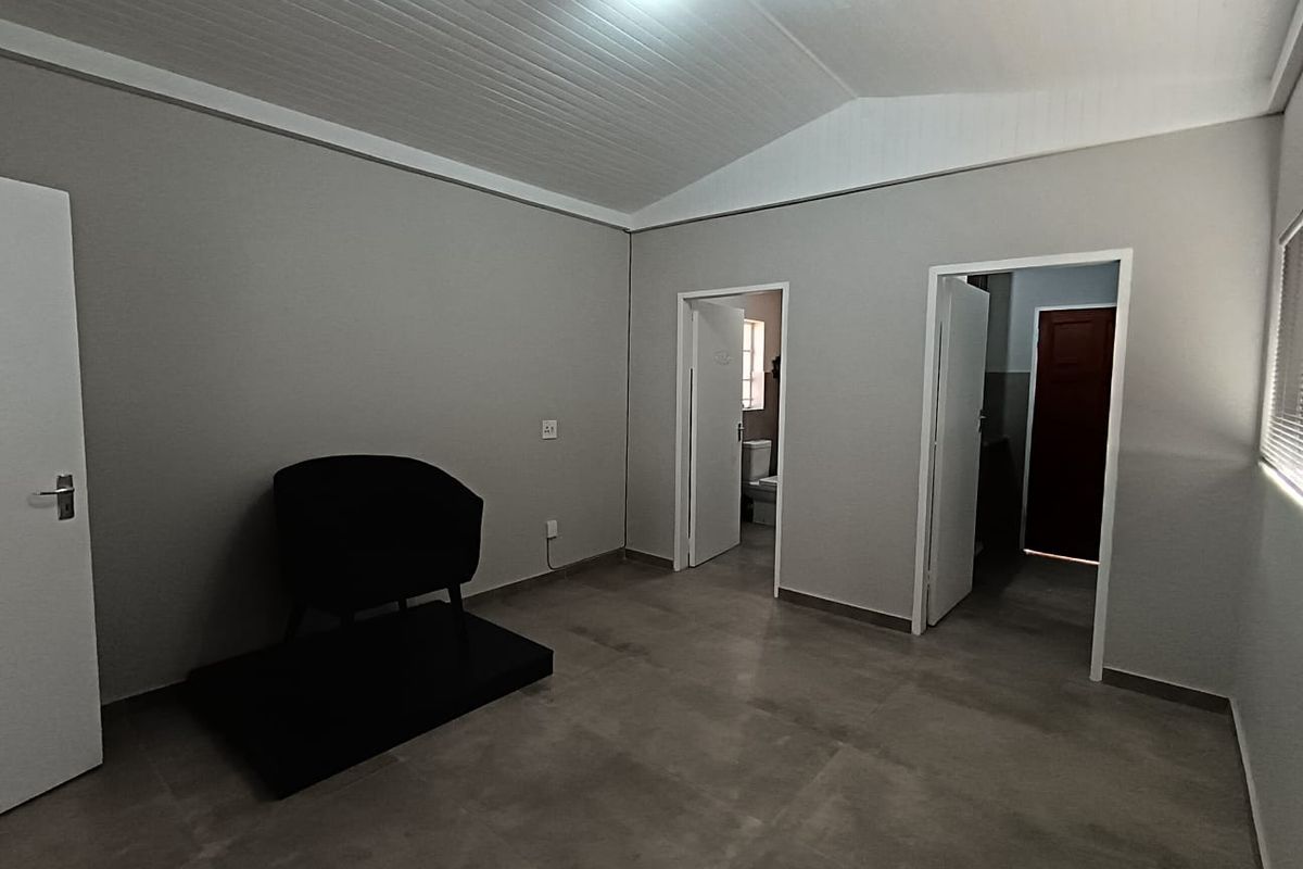 A clean, neutral-toned living area featuring tiled flooring and a vaulted tongue and groove ceiling, providing access to adjacent rooms.