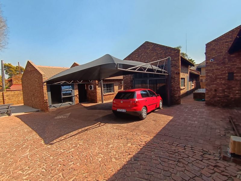 A commercial property exterior featuring a face brick facade, paved driveway, and a functional shade cloth carport structure.