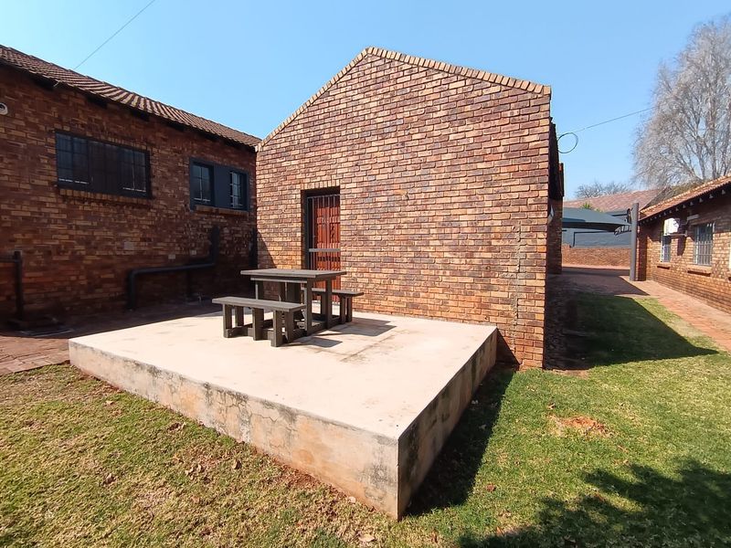 Rear exterior view of a commercial property featuring an exposed brick facade and a raised concrete patio area.