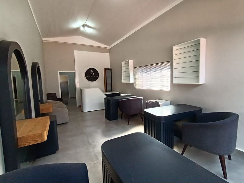 A well-maintained commercial office or salon space featuring tiled flooring, built-in reception desk, wall-mounted shelving, and neutral wall finishes.