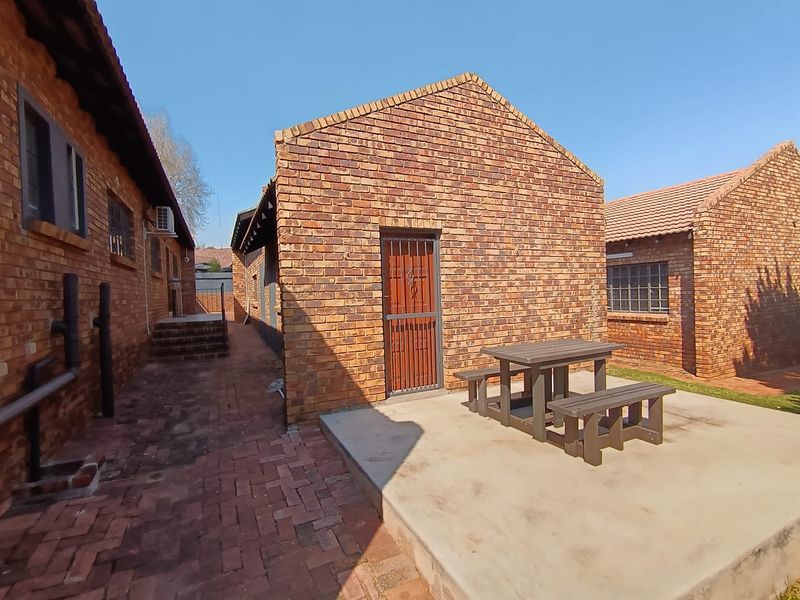 Rear exterior view of a commercial property featuring face brick construction, a concrete patio area, and paved walkways between building wings.