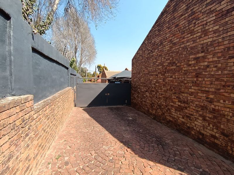 A secure entrance driveway featuring a cobblestone surface, enclosed by brick and painted perimeter walls with an integrated metal security gate.