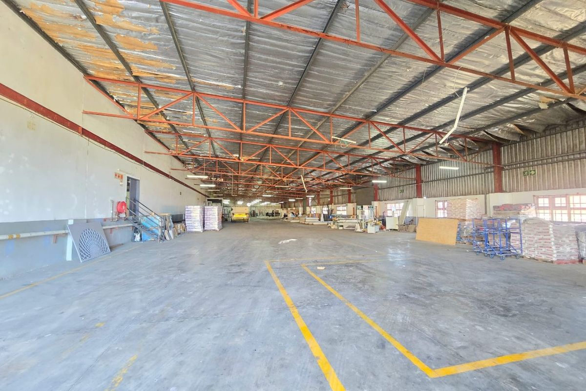 Spacious industrial warehouse featuring exposed steel roof trusses, concrete flooring, and high ceilings, suitable for various storage or manufacturing operations.