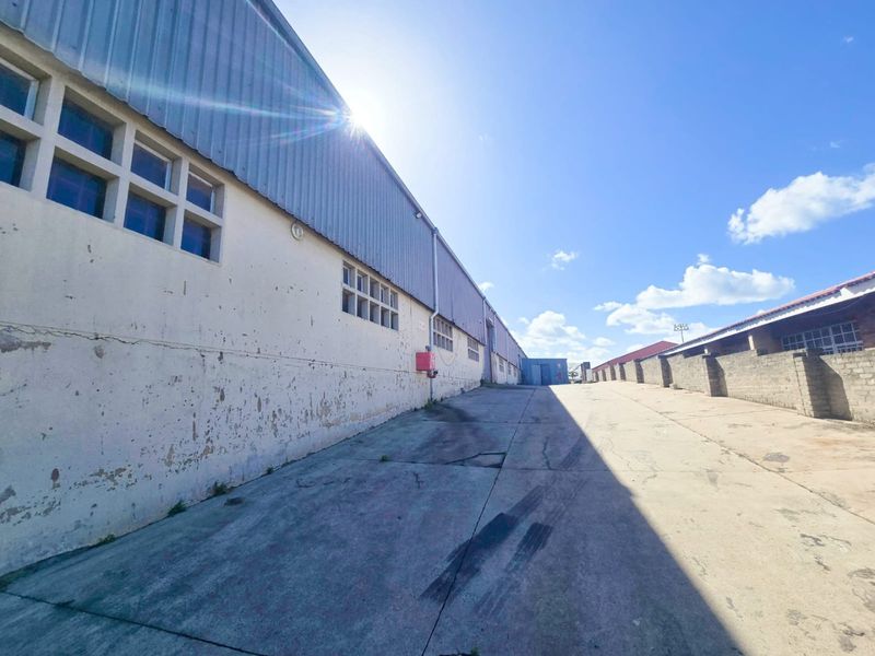 Exterior view of an industrial warehouse facility featuring corrugated metal cladding, concrete driveway, and masonry boundary walls.
