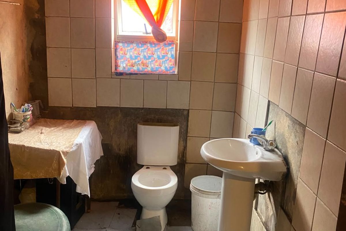 A small bathroom featuring a pedestal basin and toilet, currently requiring significant renovation and repair to wall and floor finishes.
